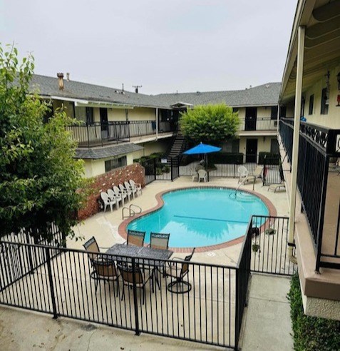 A black fence surrounds a small pool with chairs and an umbrella.