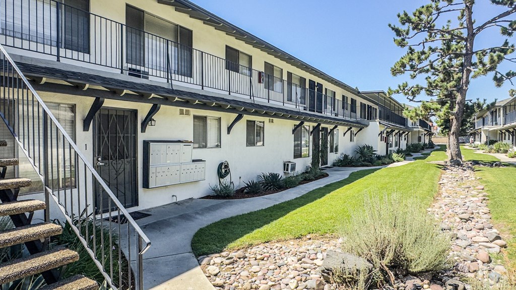 A row of white buildings with balconies and a tree in front.