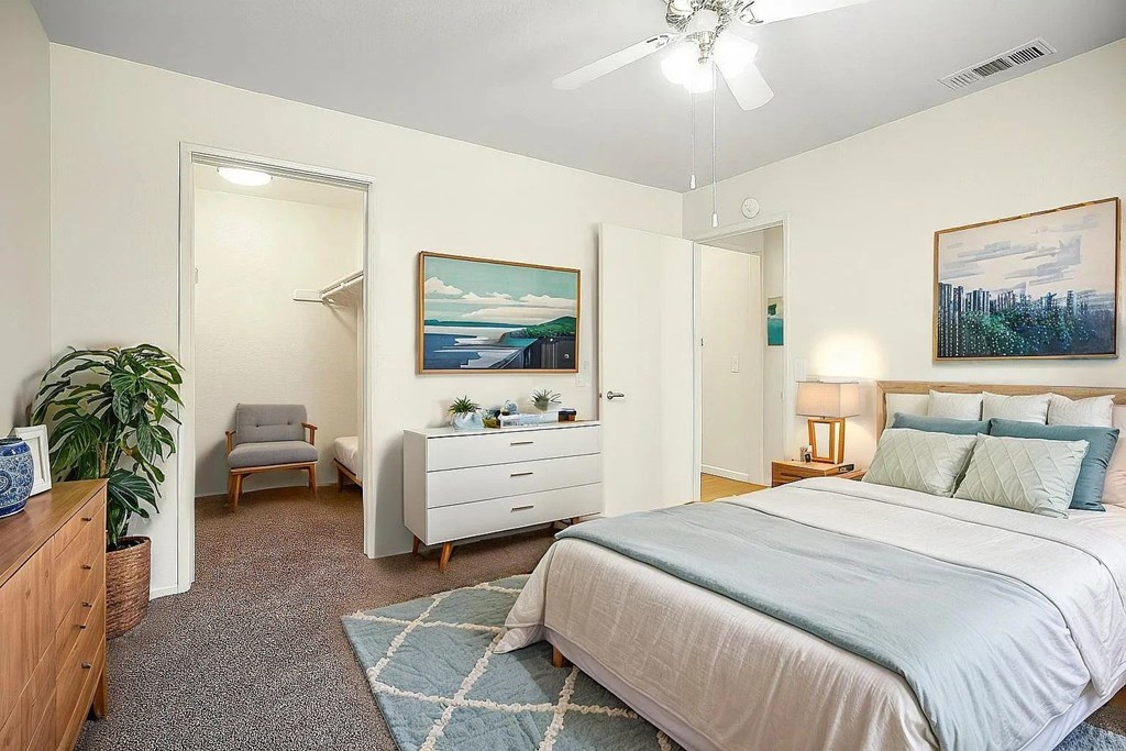 A bedroom with a bed, dresser, chair, and painting.