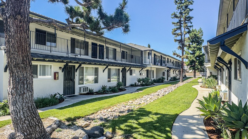 A row of white buildings with balconies and windows are lined up on a sunny day.
