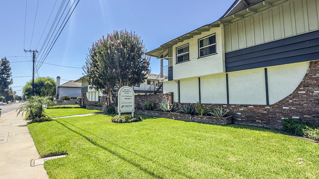 A sign in front of a house with a green lawn.