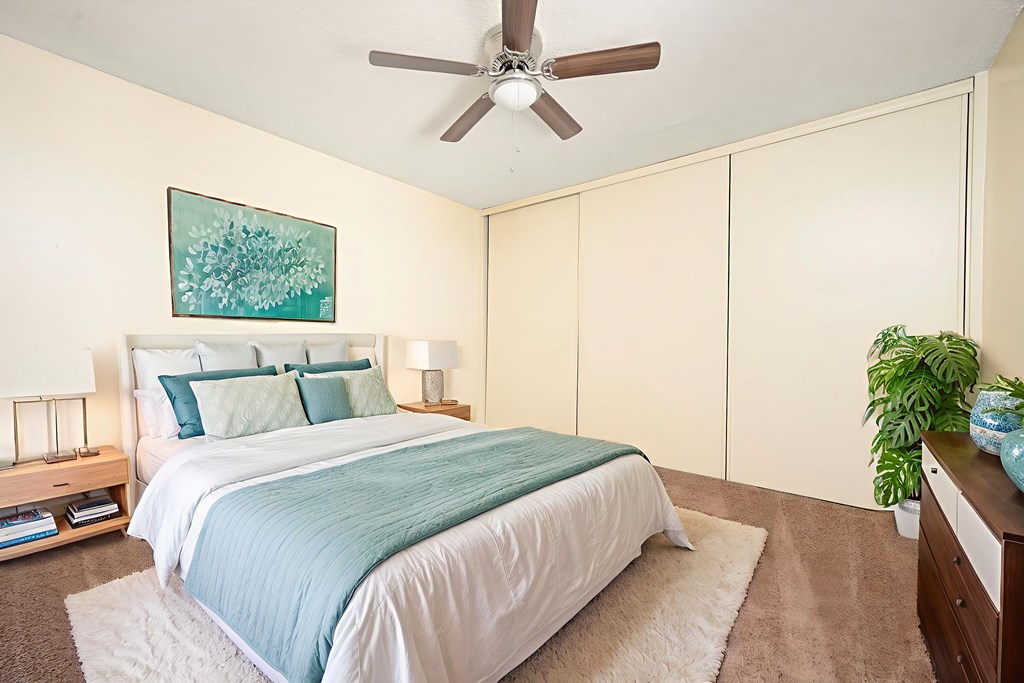 A bedroom with a bed, a ceiling fan, and a painting on the wall.