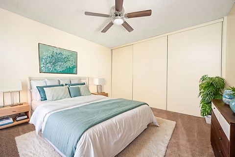 A bedroom with a bed, a ceiling fan, and a painting on the wall.