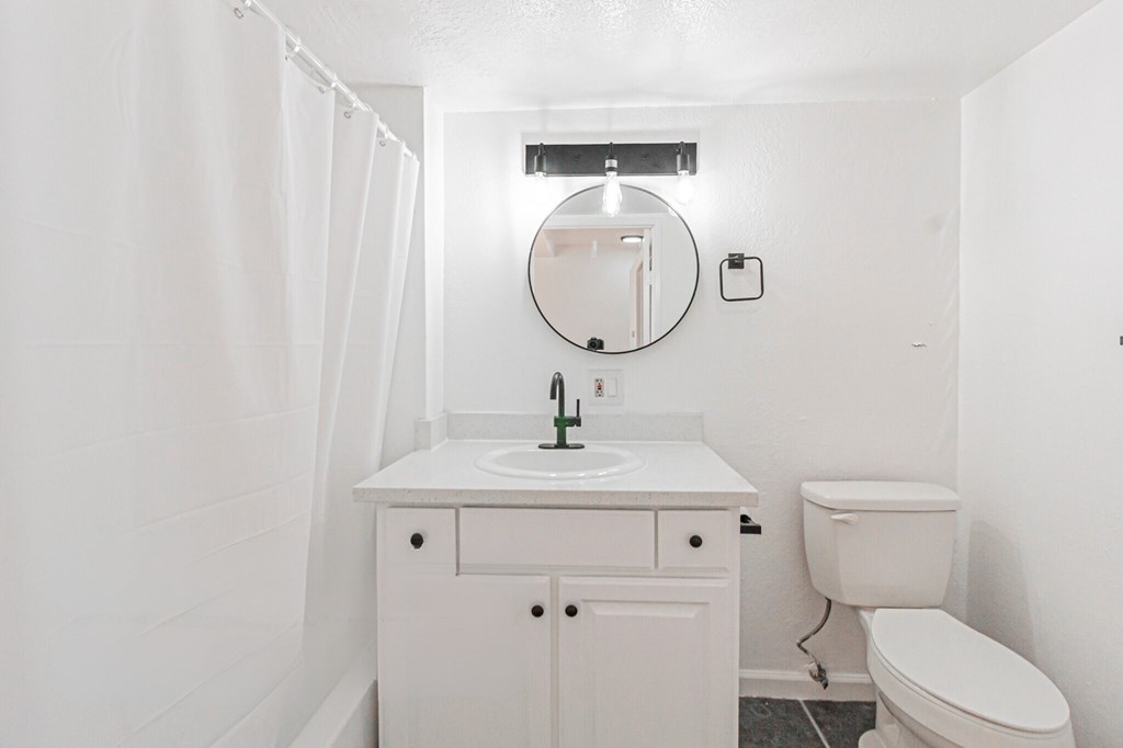 A white bathroom with a toilet, sink, and mirror.