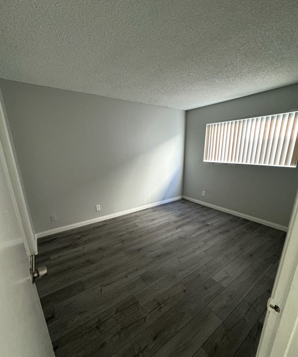 A room with wooden flooring and a window with blinds.