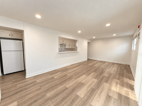 A spacious room with wooden flooring and a white refrigerator.