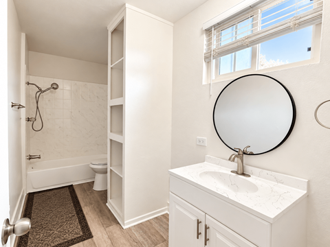 A white bathroom with a round mirror and a window.