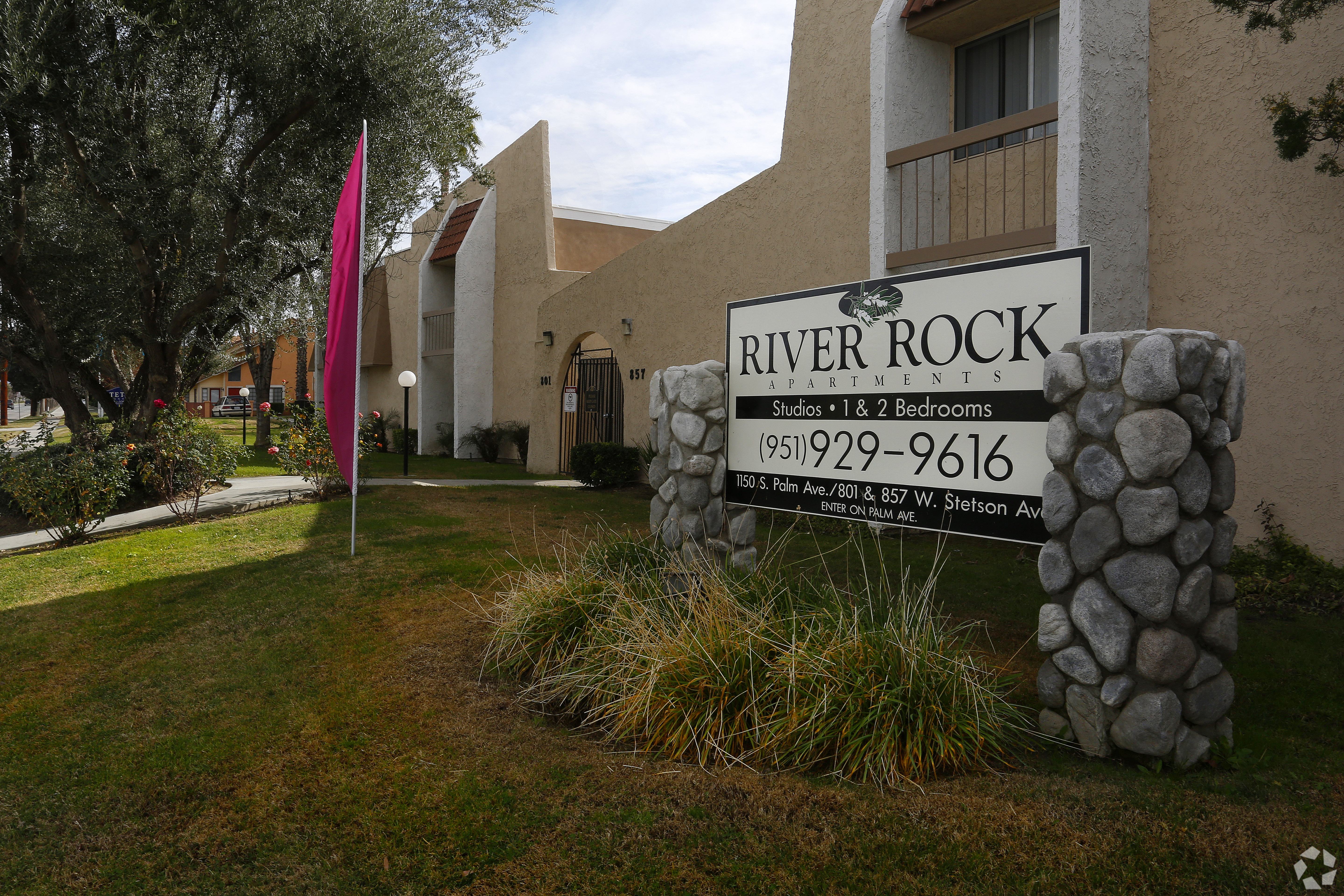 A sign for River Rock Studios and 2 Bedrooms is displayed in front of a building.