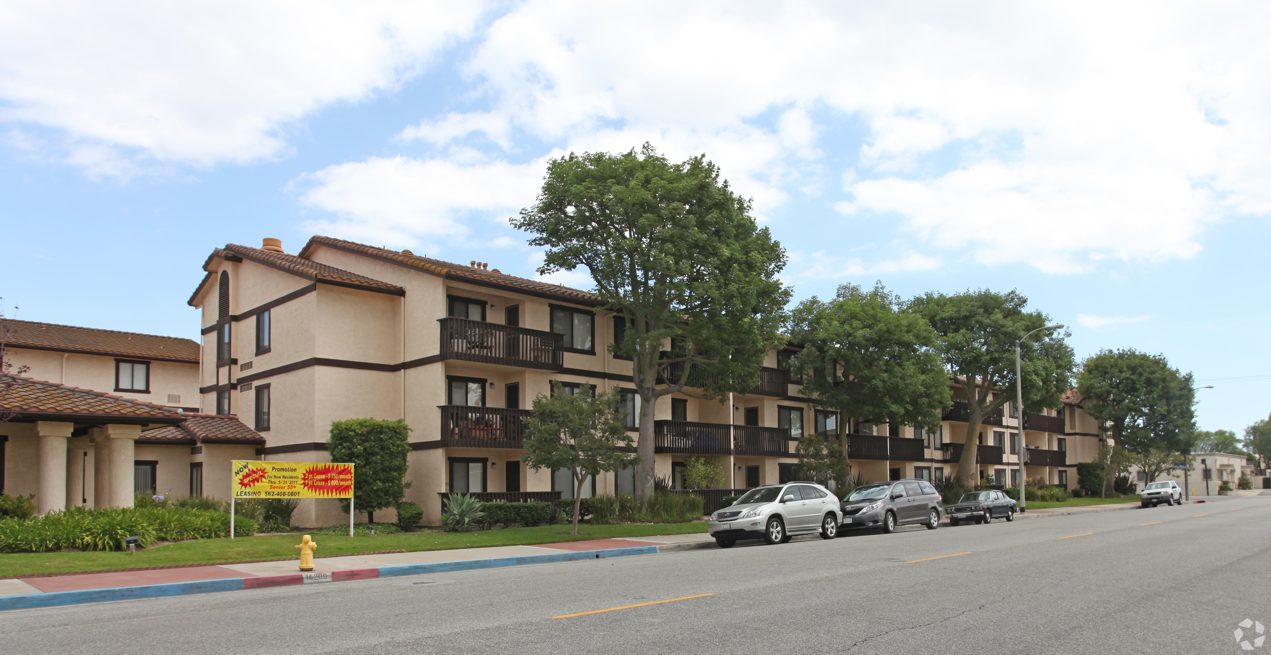 A row of apartment buildings with cars parked in front.