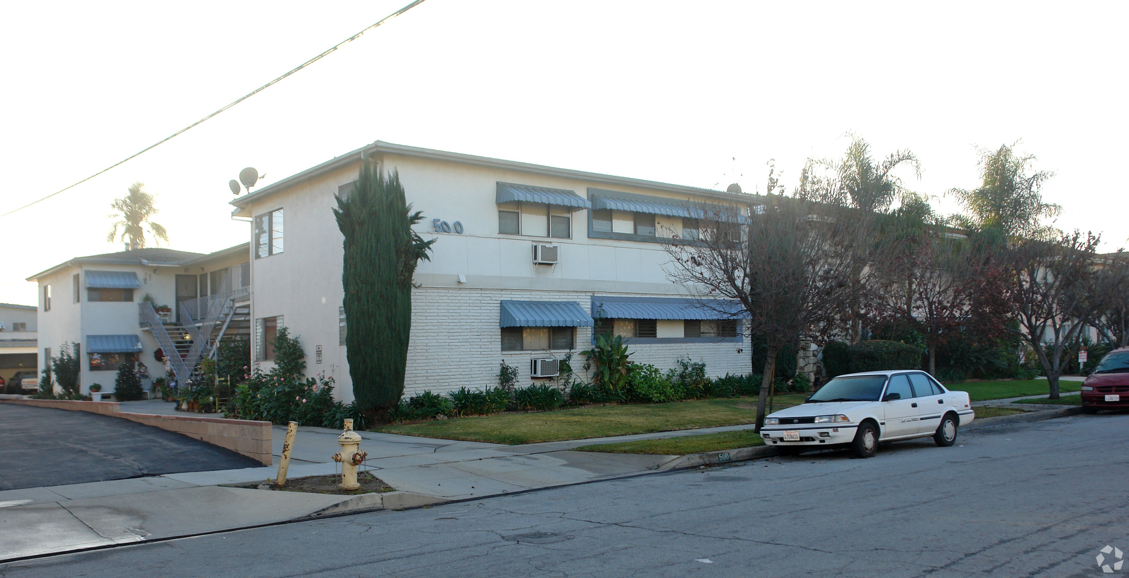 A white car is parked on the street in front of a house.