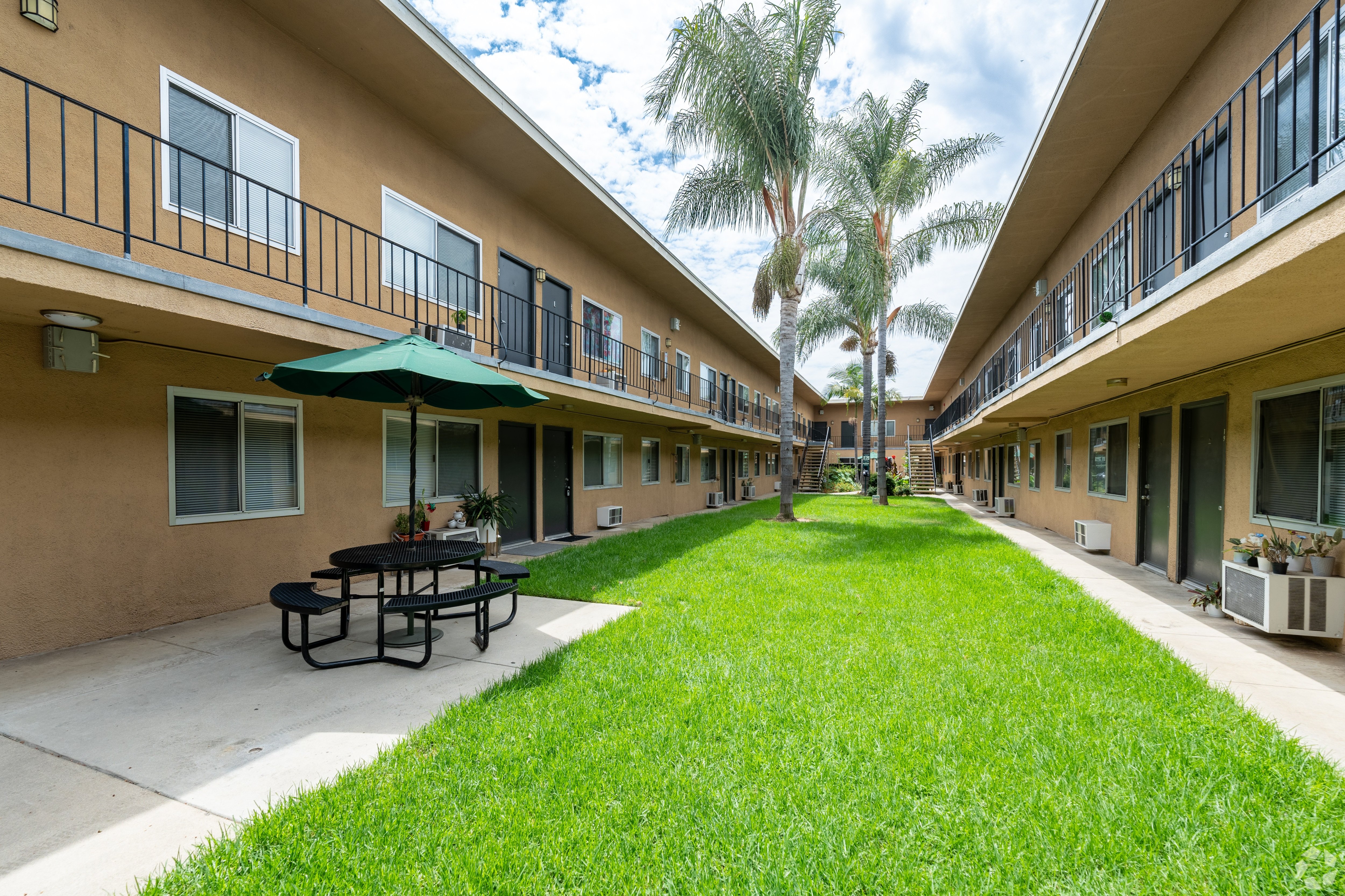 A grassy area in front of apartment buildings with a picnic table and umbrella.