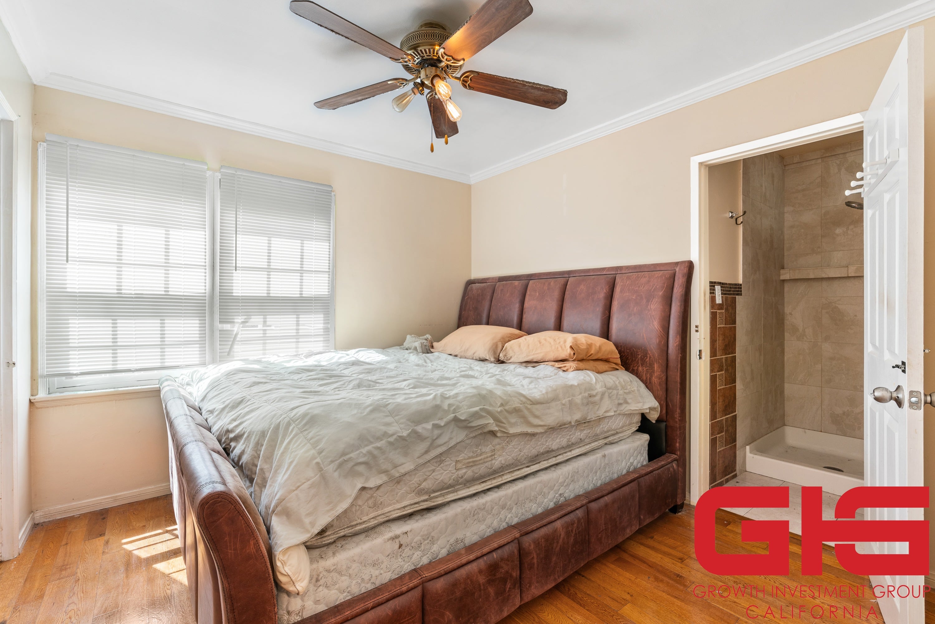 A bedroom with a bed, a ceiling fan, and a door leading to a bathroom.