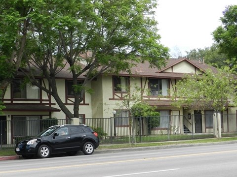 A black car is parked on the side of a street in front of a two-story house.