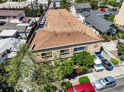 A house with a brown roof is surrounded by trees and cars.