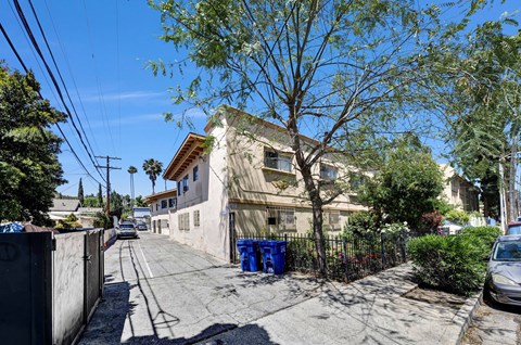 A residential street with a house, a tree, and a blue trash can.