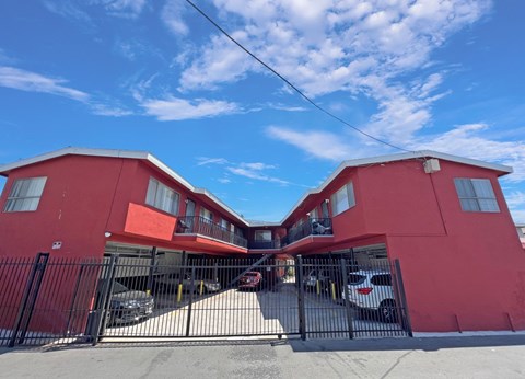 A red building with a black gate and cars parked in front.