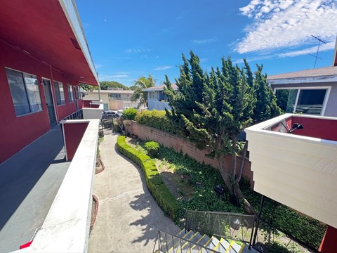 A red building with a balcony overlooking a green garden.