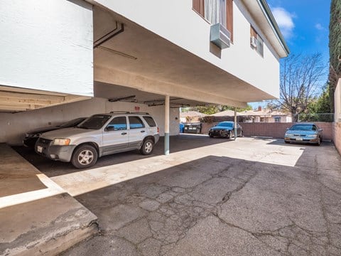 A silver car is parked in a garage under a white building.