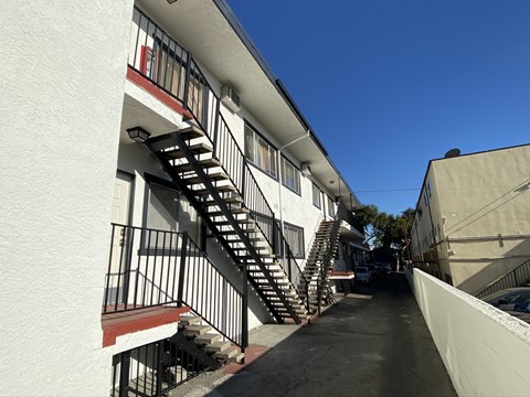 A long white building with a red stripe and a black metal staircase.
