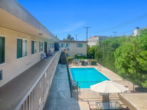 A pool with a sun lounger and umbrella is surrounded by a fence.