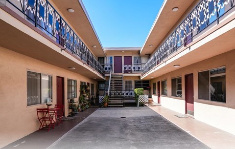 A balcony with a red table and chairs is on the left side of a building.