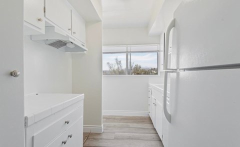 A white kitchen with a refrigerator, drawers, and a window.