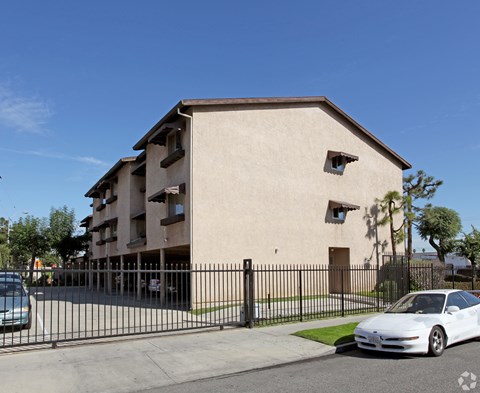 A white car is parked in front of a beige building with a black fence.
