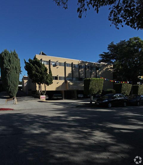 A building with a yellow facade and a sign that says "Taliesin" is surrounded by trees and has cars parked in front.