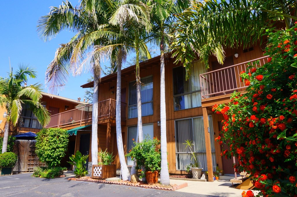 A building with a balcony and a red flower bush in front.