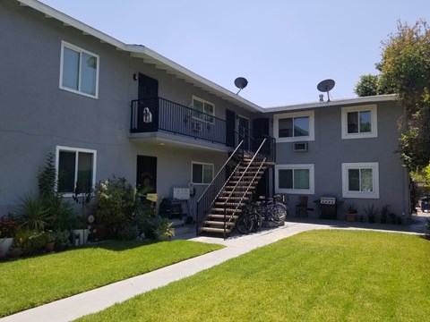 A grey two-story apartment building with a balcony and stairs leading to the second floor.