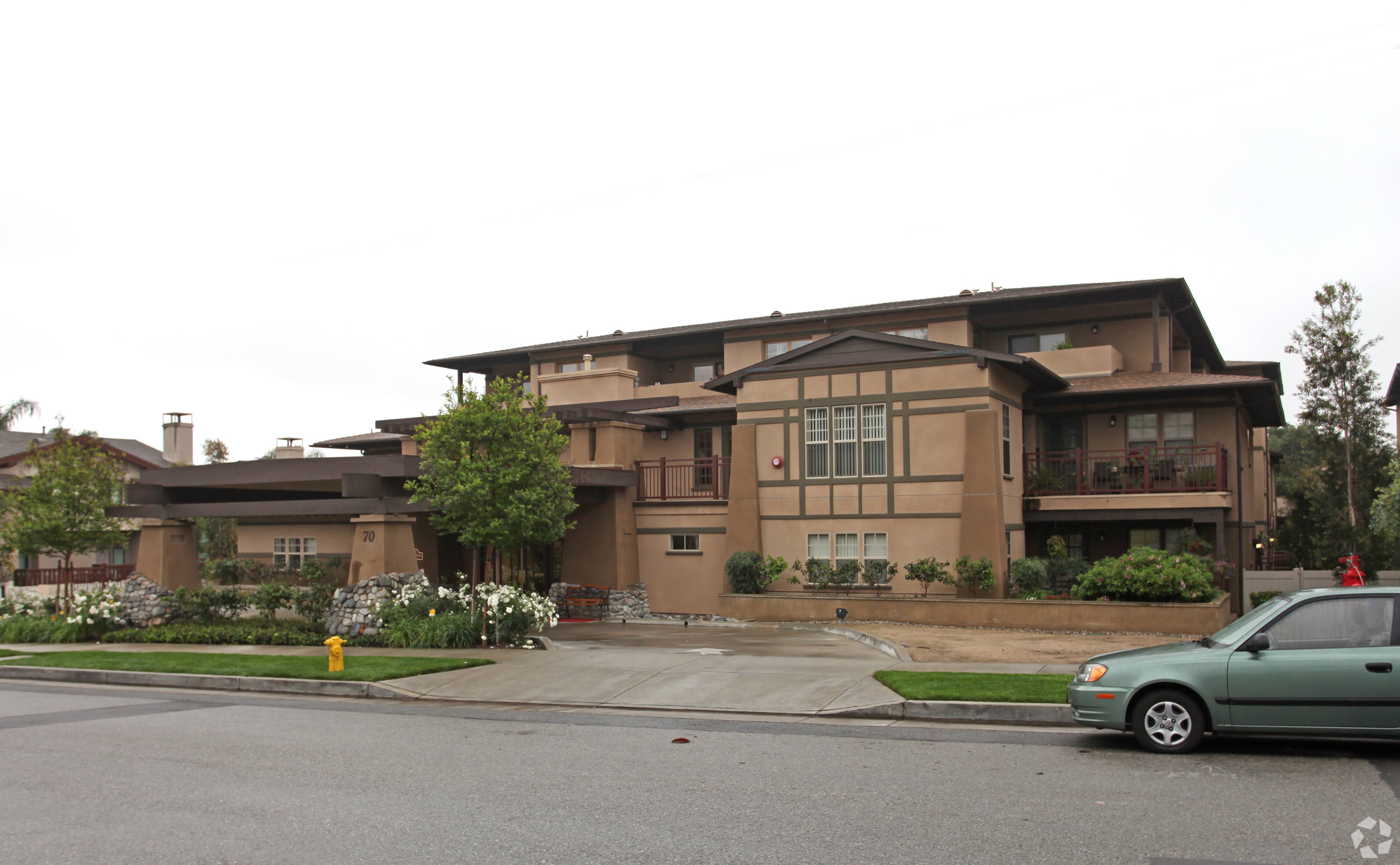 A green car is parked in front of a brown house.