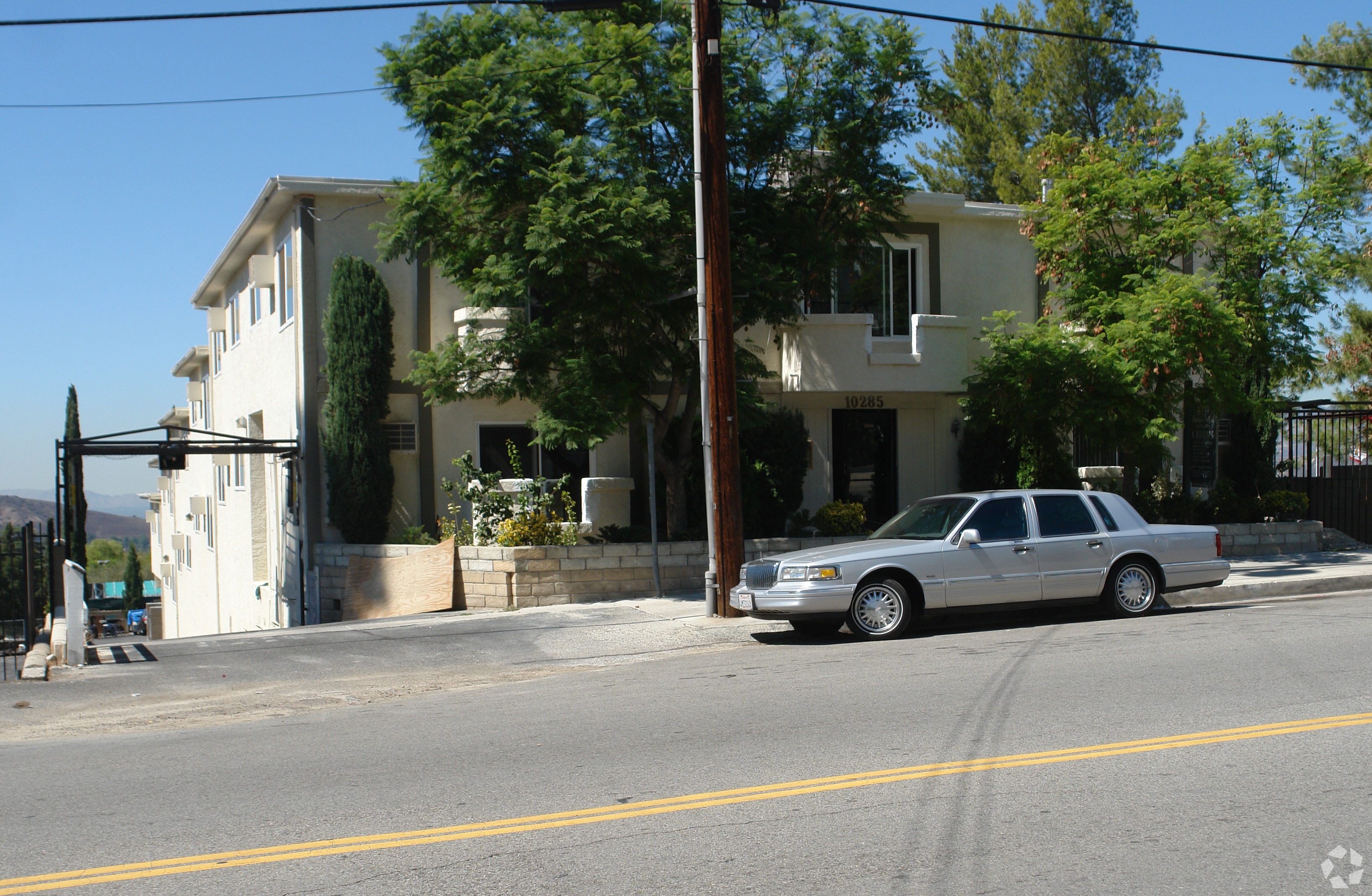 A silver car is parked on the side of a street in front of a house.