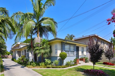 A house with a blue and yellow facade is surrounded by greenery and a clear blue sky.