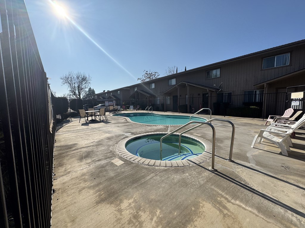 A sunny day at the pool with chairs around it.