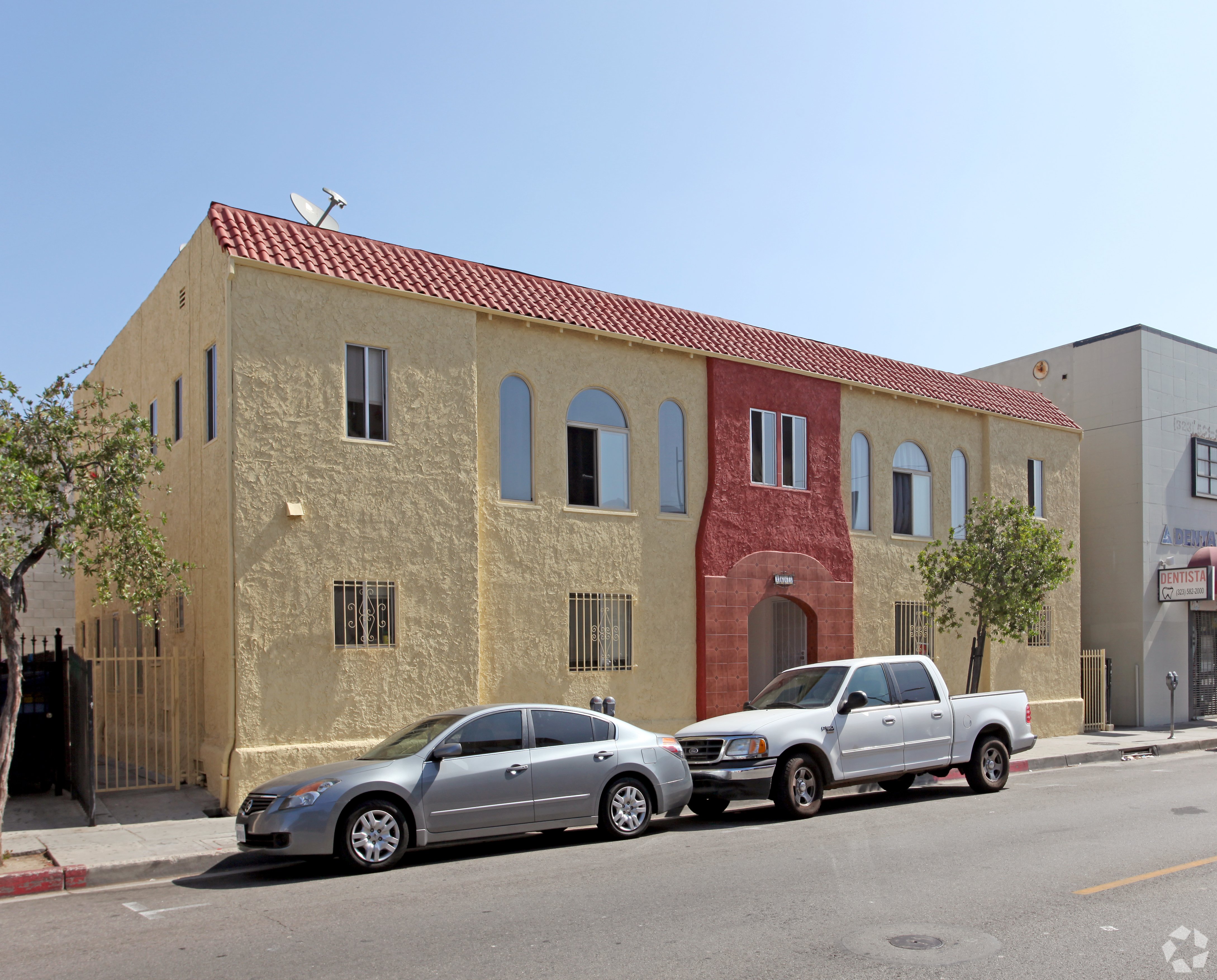 Two cars parked in front of a tan building with a red tile roof.