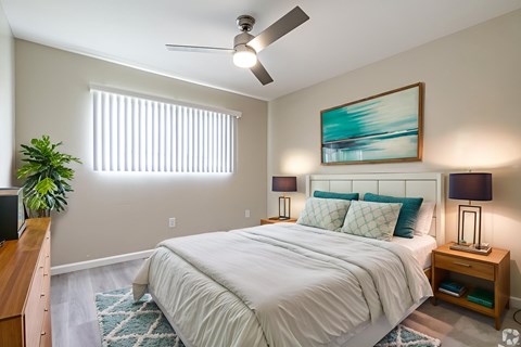 A bedroom with a large bed, a ceiling fan, and a painting on the wall.