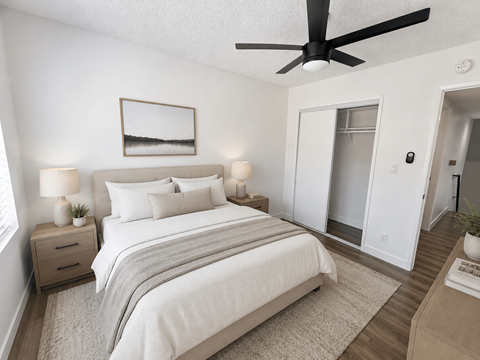 A bedroom with a large bed, a ceiling fan, and a small nightstand with a lamp.
