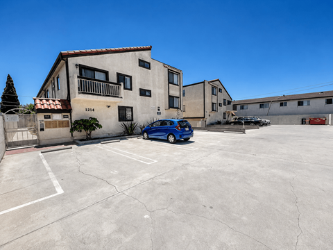 A blue car is parked in a parking lot in front of a building with the number 1214 on it.