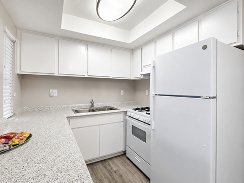 A white kitchen with a refrigerator, sink, and stove.