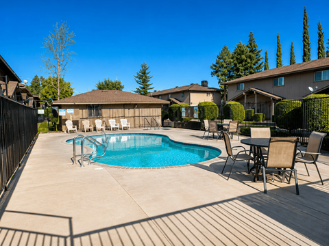 A pool surrounded by chairs and a table with a house in the background.
