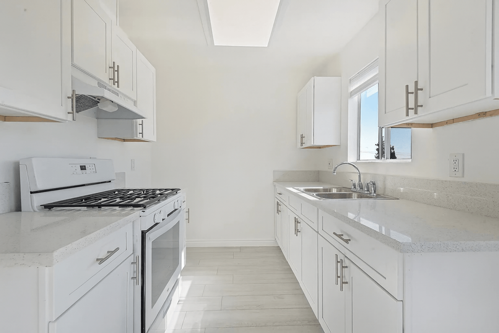 A white kitchen with a stove, sink, and cabinets.