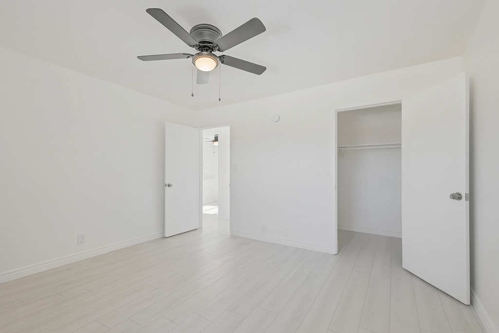 A room with a ceiling fan and white walls.