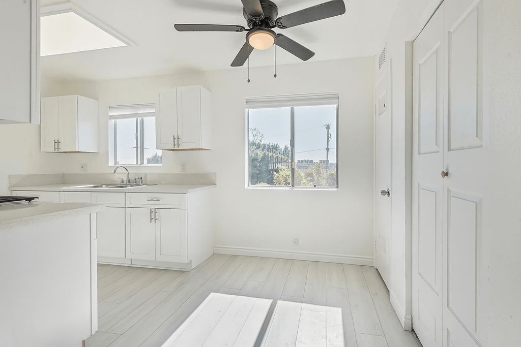 A white kitchen with a ceiling fan and a window.
