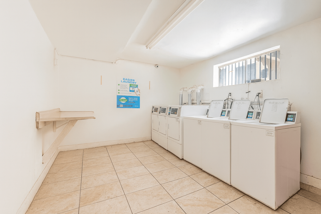 A room with a white wall and a row of washing machines.