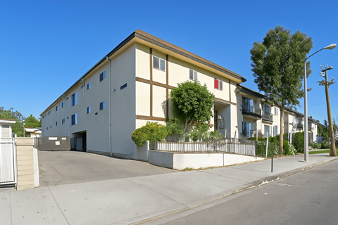 A building with a white facade and a yellow roof is surrounded by a fence and has a tree in front of it.