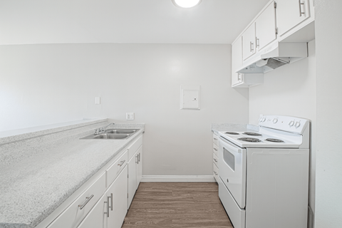 A kitchen with a stove, sink, and cabinets.