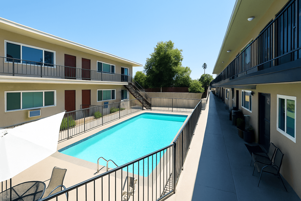 A pool in a sunny courtyard surrounded by chairs and buildings.