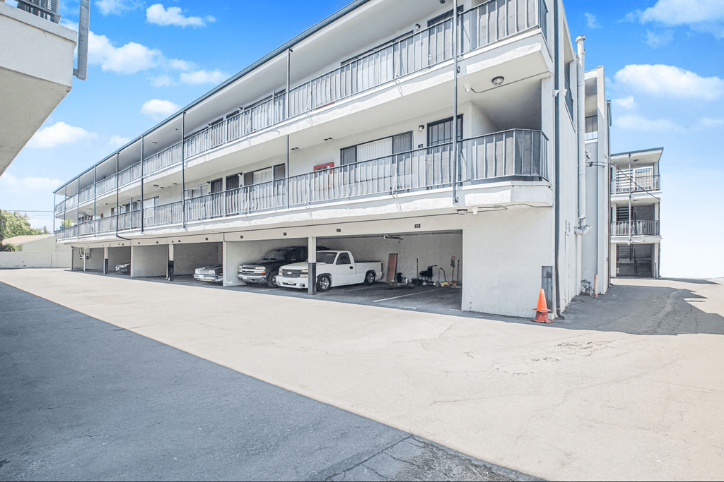 A white building with balconies and cars parked in front.