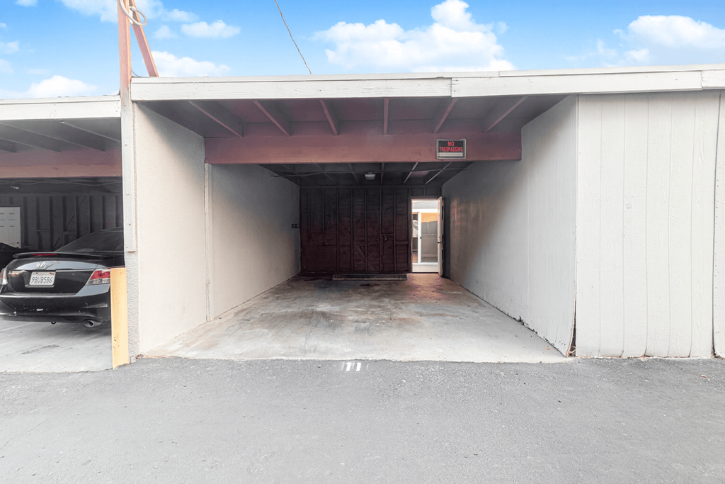 A car is parked in a garage with a white wall and a brown door.