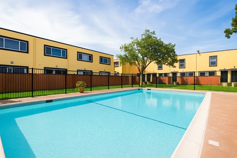 A swimming pool in front of a yellow building with black fencing.